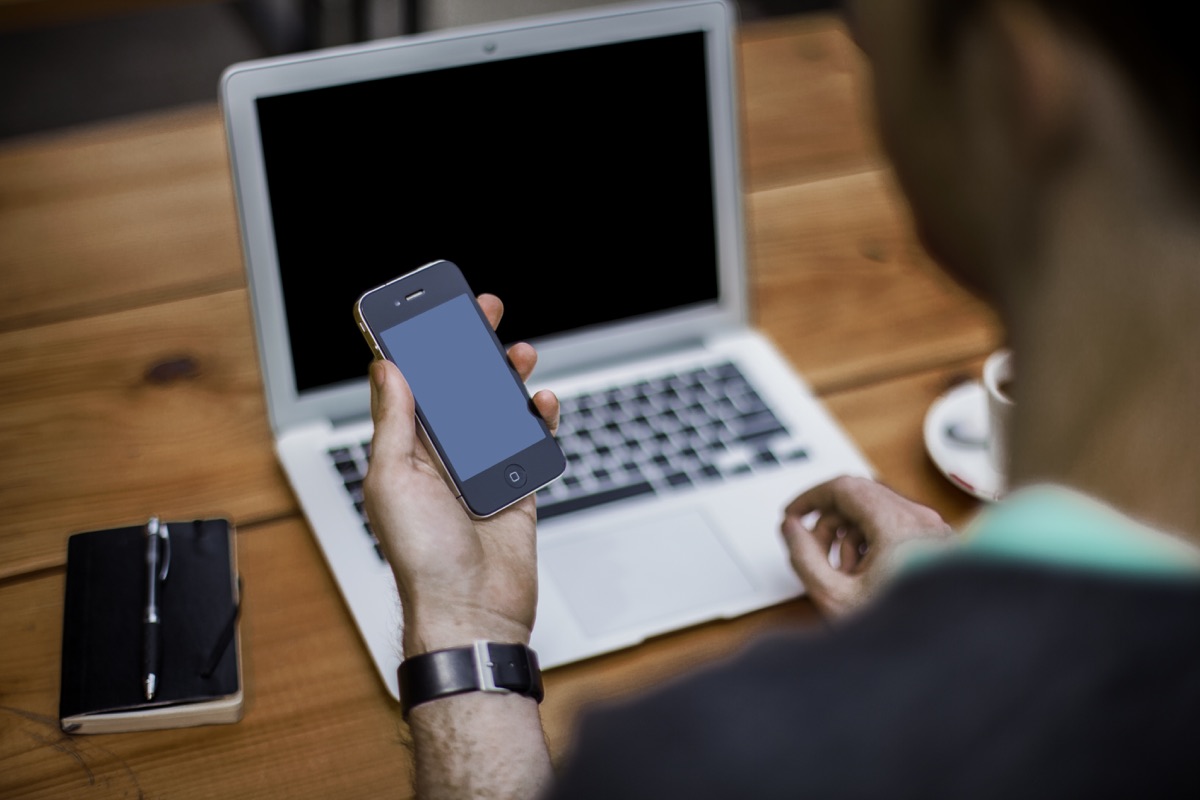 Persona revisando contenido en un teléfono junto a una laptop